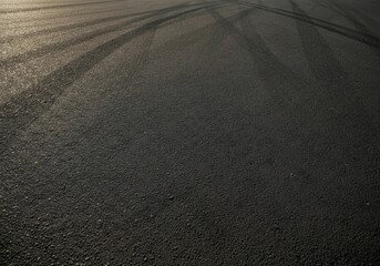 Dark asphalt surface featuring tire marks, illuminated by sunlight