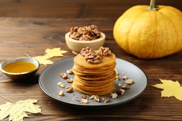 Tasty pumpkin pancakes with nuts, honey and maple leaves on wooden table