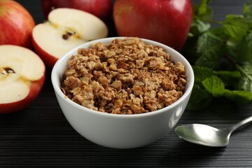 Delicious apple crisp in bowl, fresh fruits and mint on black textured table, closeup