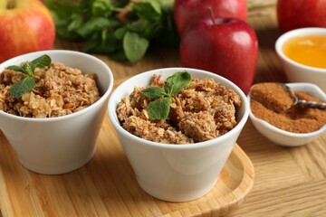 Delicious apple crisp in bowls, fresh fruits, cinnamon, mint and honey on wooden table, closeup