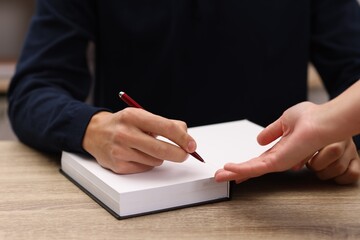 Writer signing autograph in book at wooden table indoors, closeup
