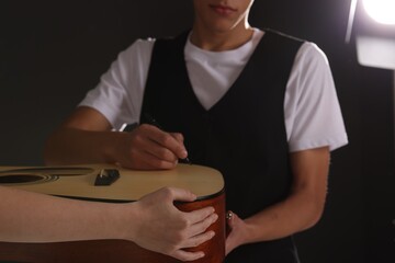 Musician signing autograph on guitar against dark background, closeup
