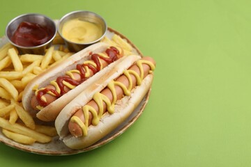 Tasty hot dogs with fries and sauces on green background, closeup. Space for text