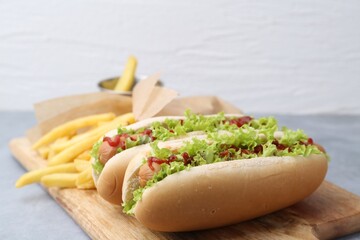 Tasty hot dogs with lettuce, ketchup and potato fries on light grey table, closeup