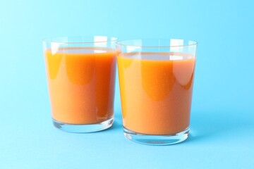 Fresh carrot smoothie in glasses on light blue background, closeup