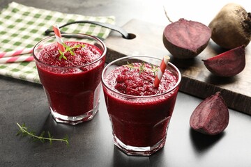Fresh beetroot smoothie in glasses and cut vegetables on grey textured table, closeup
