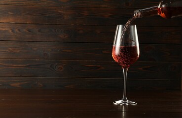 Pouring rose wine into glass at wooden table, space for text