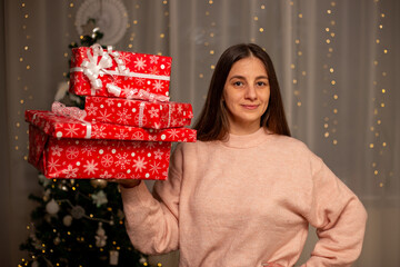 Smiling Woman Holding Christmas Gift in Light Pink Sweater by Decorated Tree, Cozy Holiday Scene with Twinkling Lights, Warm Winter Atmosphere, Festive Spirit, Joyful Christmas and New Year