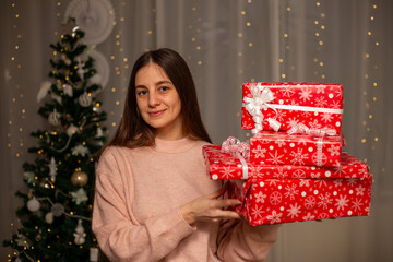 Smiling Woman Holding Christmas Gift in Light Pink Sweater by Decorated Tree, Cozy Holiday Scene with Twinkling Lights, Warm Winter Atmosphere, Festive Spirit, Joyful Christmas and New Year