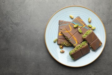 Pieces of Dubai chocolate bar with pistachios and knafeh on grey table, top view. Space for text