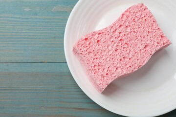 Pink sponge with foam and plate on light blue wooden table, top view. Space for text