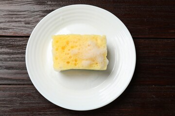 Yellow sponge with foam and plate on wooden table, top view