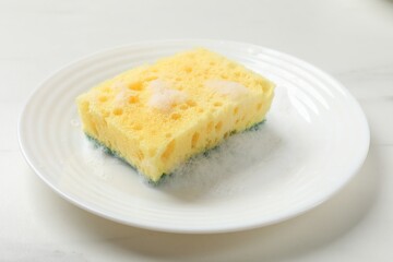 Yellow sponge with foam and plate on white table, closeup
