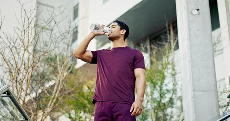 Fotobehang Man, drinking water and city athlete on break, liquid nutrition and sports drink for fitness. Male person, relax and bottle of h2o for refreshing rest in urban town, training and exercise recovery © peopleimages.com