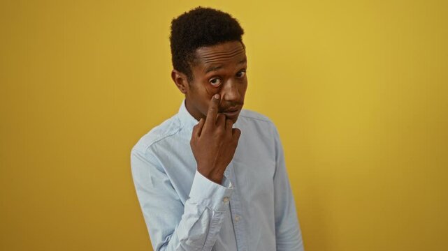 Young african american man wearing shirt standing, you watching gesture pointing eye expression suspicious over isolated yellow background, exploring emotions of trust and awareness