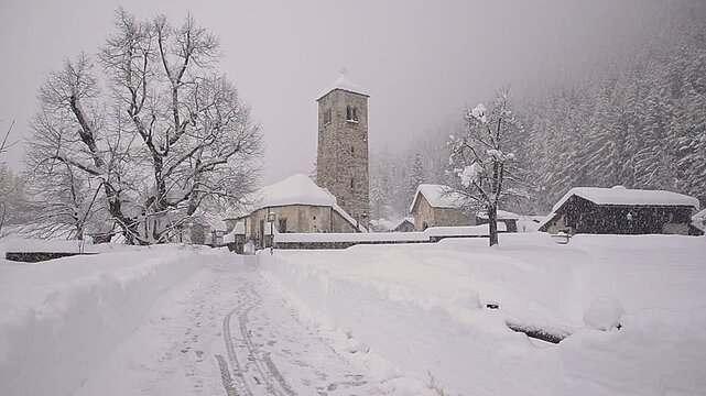 Picturesque and characteristic mountain church during a heavy snowfall. Macugnaga, Italy. Tourist resort in the European Alps in winter at the foot of Monte Rosa, Piedmont region