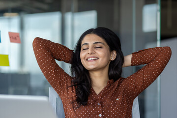 Smiling businesswoman leaning back at her workplace, embodying relaxation and contentment in a...