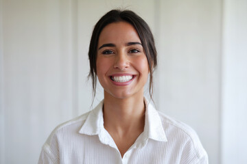 Mujer morena mirando a cámara y sonriendo con una dentadura perfecta. Camisa blanca y fondo blanco. Generado con IA