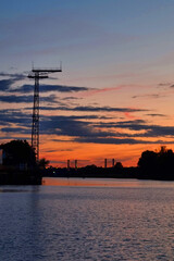 Naklejka premium Serene Sunset over River with Bridge Silhouette and Transmission Tower
