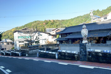 A large porcelain vase with bright patterns, placed in front of Hasami town's wooden buildings and peaceful surroundings. Traditional porcelain production in Japan.