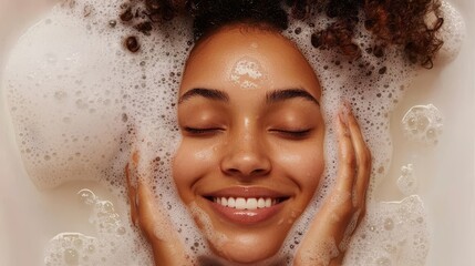 A young woman with a smile cleanses her face with a natural, foamy gel. The happy girl, with bare shoulders, applies a beauty product to her cheeks and closes her eyes. This is a regular part of her
