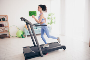 Fototapeta premium Energetic woman running on treadmill in bright modern home interior with natural light
