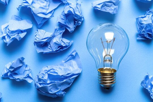 A bright light bulb surrounded by crumpled blue paper, often used for creative or brainstorming purposes