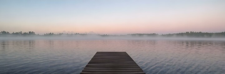 Fototapeta premium A peaceful evening view of a wooden dock on a misty lake, with soft ripples reflecting a pastel sunset.