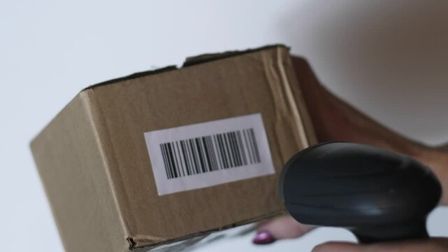 close-up of a parcel being scanned with a barcode scanner, a female employee of a pick-up point or logistics center, a box with goods being scanned by barcode