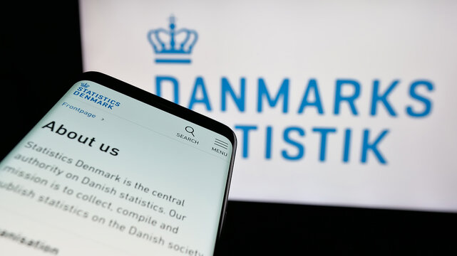 Stuttgart, Germany - 11-24-2024: Mobile phone with website of Danmarks Statistik (Statistics Danmark, DST) on screen in front of logo. Focus on top-left of phone display.