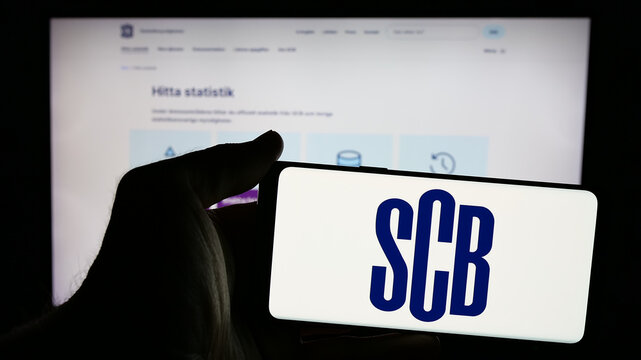 Stuttgart, Germany - 11-24-2024: Person holding mobile phone with logo of Statistiska Centralbyran (Statistics Sweden, SCB) on screen in front of web page. Focus on phone display.