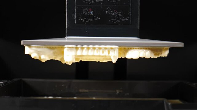 3d printer creates a set of human teeth for dentistry, slowly lowering them into a vat of liquid. This innovative process showcases advancements in dental technology and manufacturing. 4 k video