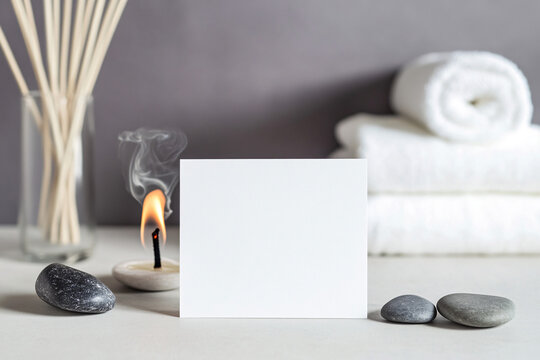 A blank invitation card rests on a serene table setup surrounded by smooth stones, a burning candle, and neatly rolled towels in a calming environment