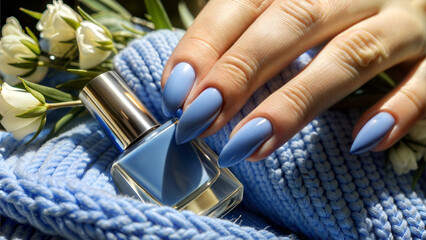 Close-up of female hands with blue manicure holding a perfume bottle on a knitted scarf