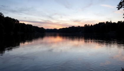 Calm lake at sunset reflecting colorful sky and trees under tranquil atmosphere