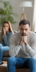 Obraz premium A man and woman are sitting on a couch in a living room. The man is looking down and he is upset. The woman is looking at him, but her expression is not clear. Scene is tense and emotional