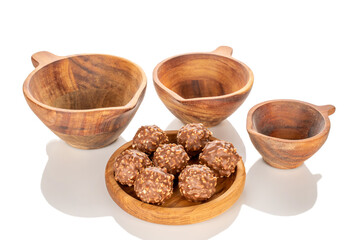 Chocolate candies with hazelnuts in a wooden bowl, close-up, isolated on a white background.