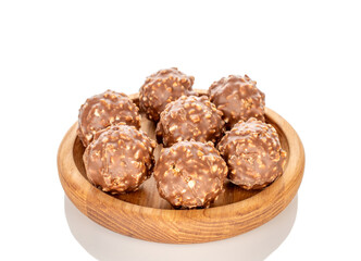 Chocolate candies with hazelnuts in a wooden bowl, close-up, isolated on a white background.