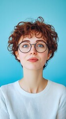 Obraz premium Surprised young woman with curly hair and glasses expressing amazement against a bright blue background