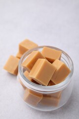 Tasty sweet caramel candies in glass jar on light table, closeup