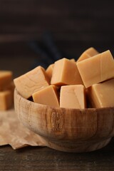 Tasty sweet caramel candies in bowl on wooden table, closeup