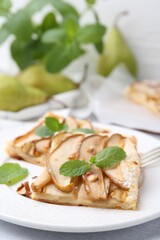 Pieces of tasty puff pastry pie with pears and mint on table, closeup