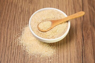 Oat bran in bowl and spoon on wooden table, closeup