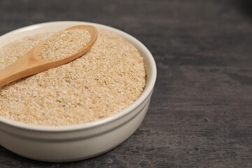 Oat bran in bowl and spoon on grey table, closeup. Space for text