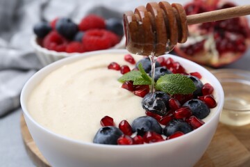 Pouring honey onto tasty cooked semolina porridge at table, closeup