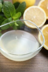 Fresh lemon juice in bowl, fruits and mint on wooden table, closeup