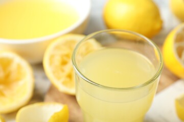Glass of fresh lemon juice and squeezed fruits on table, closeup