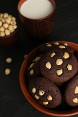 Tasty chocolate cookies with hazelnuts and milk on black table, closeup