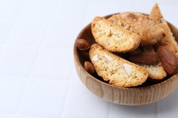 Tasty almond biscuits (Cantuccini) and nuts in bowl on white tiled table, closeup. Space for text