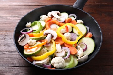 Frying pan with mix of vegetables and mushrooms on wooden table, closeup